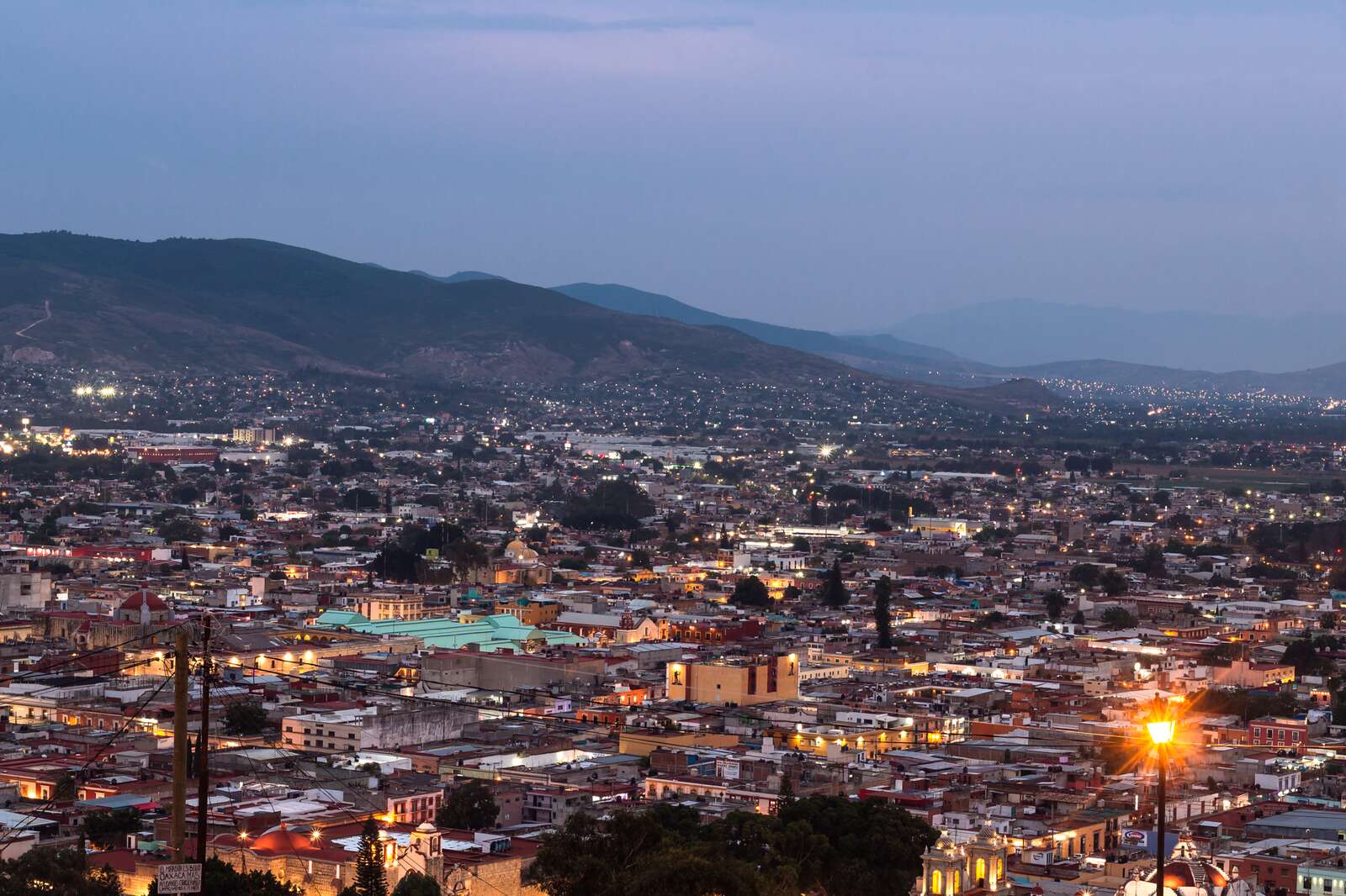 A city at dusk with its lights coming on below a mountain backdrop