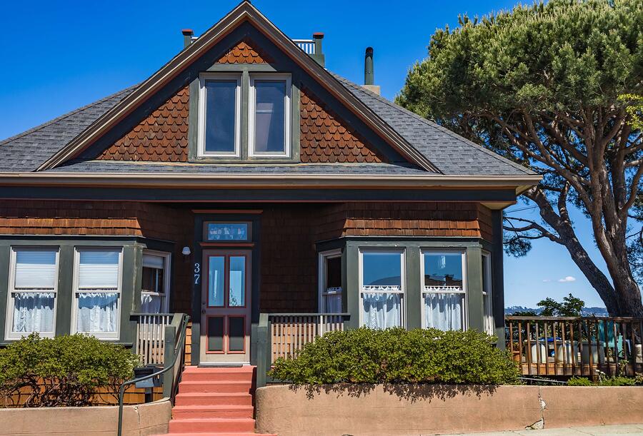 An older wood-frame house with a deep porch and a mature tree touching the roofline