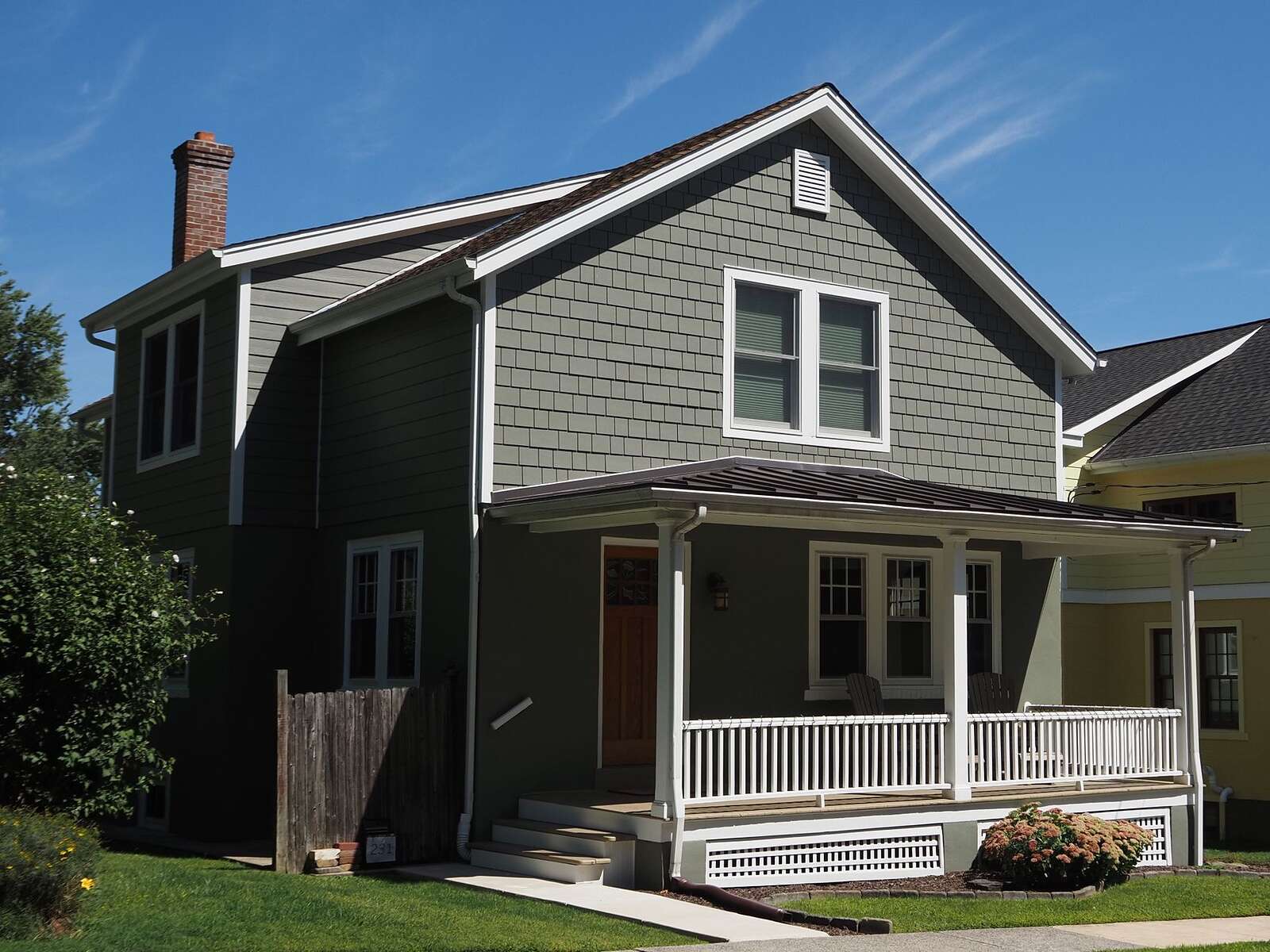 A gray single-family house with a front porch and open eaves under a clear sky