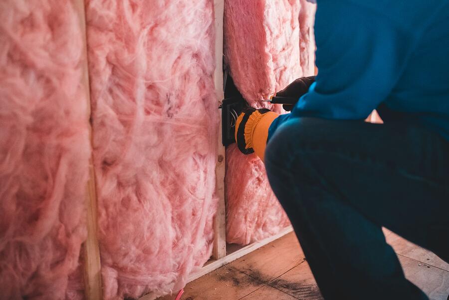Gloved hands fitting pink insulation batts between wall studs